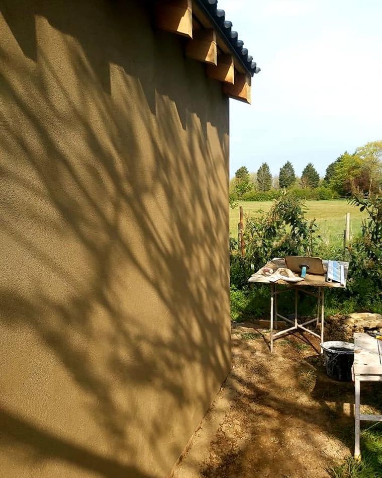 Smooth sand-coloured render on a gable end with tree shadows across the wall