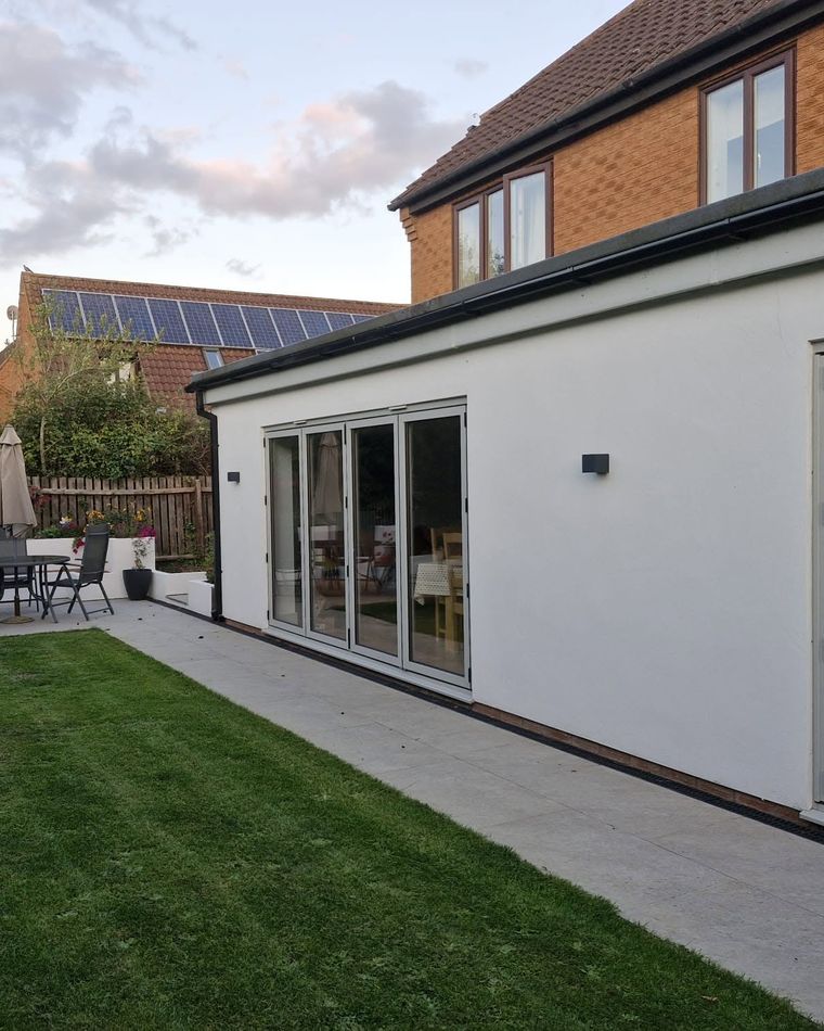 White rendered house extension with bifold doors and a lawn